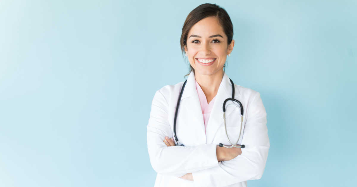 smiling female doctor in lab coat with arms crossed against blue background